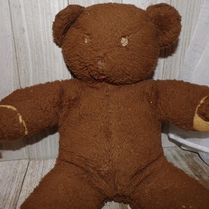 May include: A brown teddy bear with a worn, fuzzy texture. The bear has a stitched nose and missing fur on its paws.