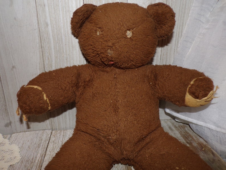 May include: A brown teddy bear with a worn, fuzzy texture. The bear has a stitched nose and missing fur on its paws.