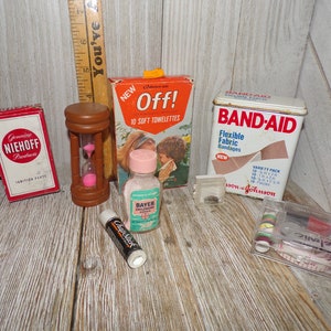 May include: A collection of vintage items including a red and white box labeled "Genuine Niehoff Products", a wooden hourglass with pink sand, a small bottle of Bayer Children's Aspirin, a red and white box labeled "Off! 10 Soft Towelettes", a tin of Band-Aid Flexible Fabric Bandages, a clear plastic container with spools of thread, and a red and white ChapStick.