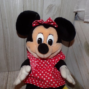 K&ouml;nnte beinhalten: Ein Pl&uuml;schtier von Minnie Mouse, das ein rotes Kleid mit wei&szlig;en Punkten und eine rote Schleife tr&auml;gt. Das Spielzeug hat schwarze Ohren und eine schwarze Nase.