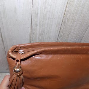 May include: A brown leather clutch bag with a tassel zipper pull.