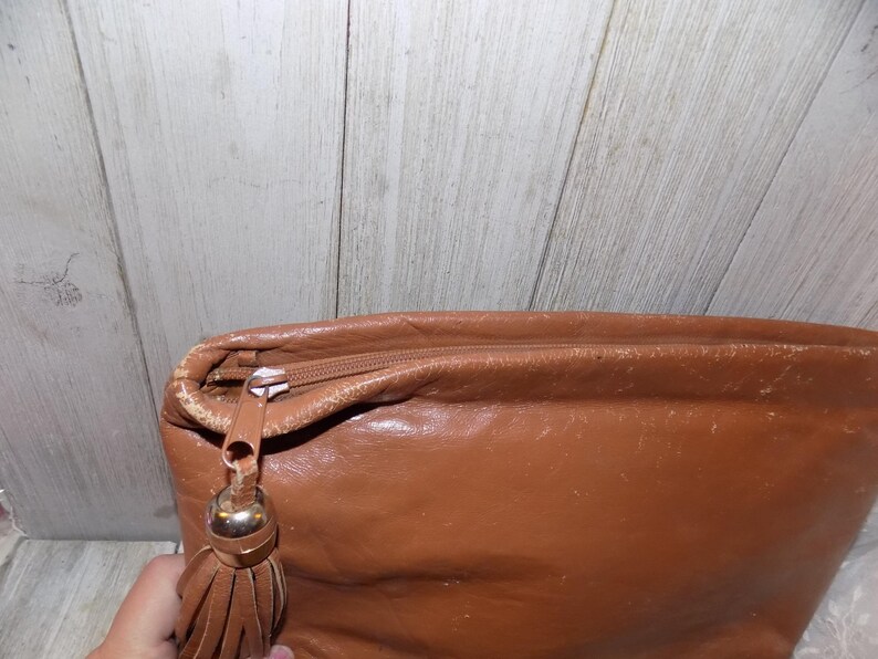 May include: A brown leather clutch bag with a tassel zipper pull.