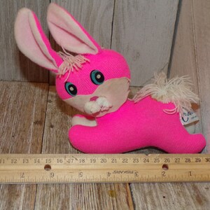 May include: Pink plush bunny rabbit toy with white ears and a white fluffy tail. The bunny has blue eyes and a white nose and mouth. The toy is approximately 10 inches long.