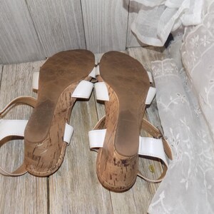 K&ouml;nnte beinhalten: Ein Paar wei&szlig;e Keilsandalen mit Korksohlen. Die Sandalen haben Kn&ouml;chelriemen und sind offen.