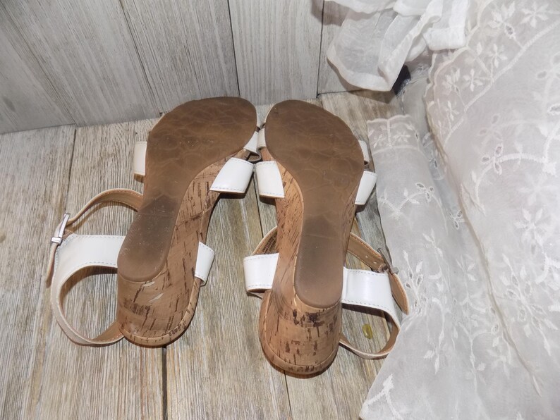 K&ouml;nnte beinhalten: Ein Paar wei&szlig;e Keilsandalen mit Korksohlen. Die Sandalen haben Kn&ouml;chelriemen und sind offen.