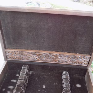 May include: Open wooden silverware chest with a dark brown velvet interior. The inside has slots for utensils. The top of the chest has a decorative carved design with a crown in the center. The exterior is a medium brown color.