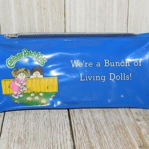 May include: Blue vinyl zippered pencil case with a Cabbage Patch Kids logo and the text "We're a bunch of Living Dolls!"  The logo features two Cabbage Patch Kids dolls, one watering a patch of cabbages.
