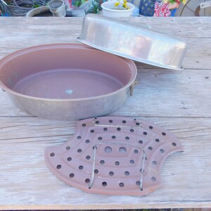 May include: A vintage, oval-shaped, aluminum roaster with a lid and a removable, perforated rack. The roaster is brown and the rack is silver.