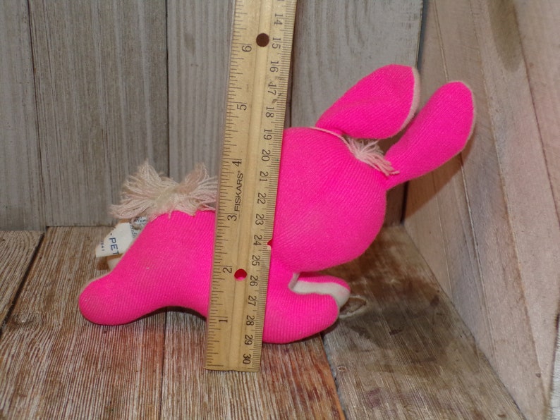 May include: A pink plush bunny toy with white fur accents. The bunny is lying on its side with its head turned to the right. The toy is approximately 7 inches long.
