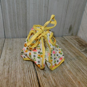 May include: A yellow and white floral print doll dress with yellow trim and ties. The dress is tied at the back.