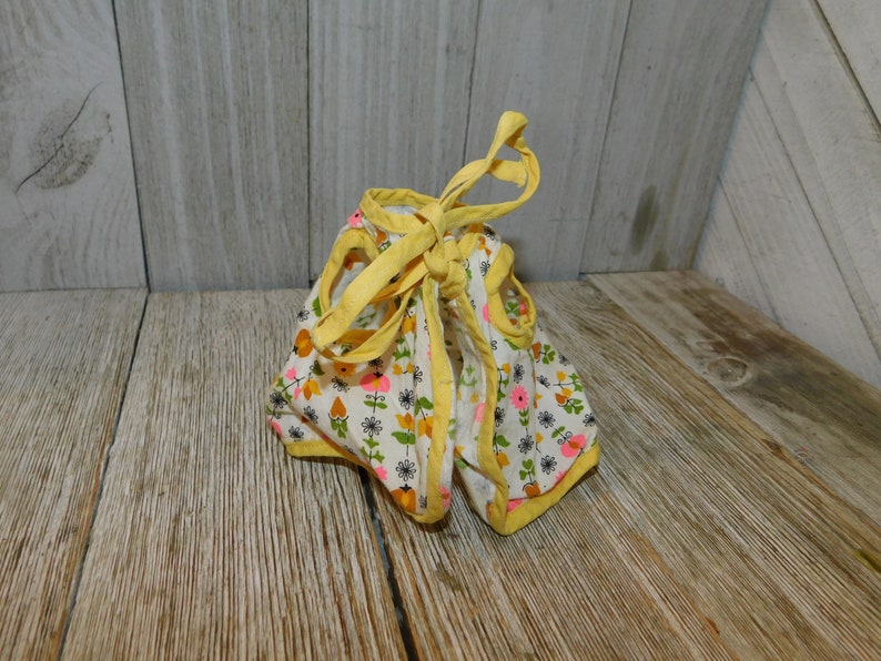 May include: A yellow and white floral print doll dress with yellow trim and ties. The dress is tied at the back.