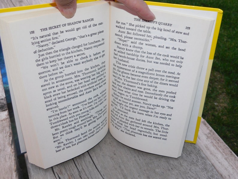 May include: Open book with yellow pages showing a scene from a novel. The text on the page reads "The Secret of Shadow Ranch" and "The Sheriff's Quarry".