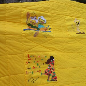 May include: Yellow quilted blanket with embroidered cartoon figures and text. Features a couple in a boat, a cartoon bird, and a couple embracing. The text reads "Love is the most fun you can have without laughing."