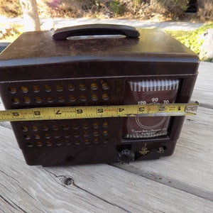 Puede incluir: Una radio-fon&oacute;grafo Emerson vintage marr&oacute;n con asa. La radio tiene un dial con n&uacute;meros y un bot&oacute;n de sintonizaci&oacute;n. La radio mide aproximadamente 25 cm de ancho.