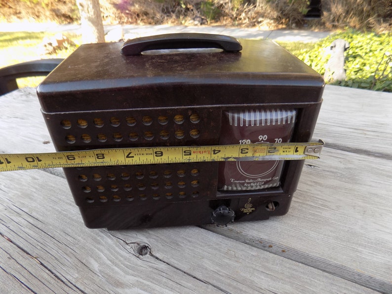 Puede incluir: Una radio-fon&oacute;grafo Emerson vintage marr&oacute;n con asa. La radio tiene un dial con n&uacute;meros y un bot&oacute;n de sintonizaci&oacute;n. La radio mide aproximadamente 25 cm de ancho.