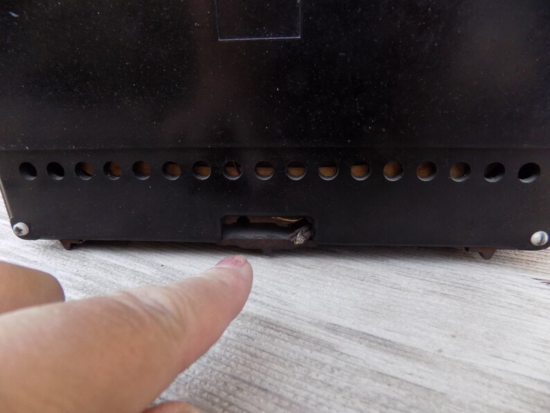 Puede incluir: Primer plano de la parte trasera de una radio vintage negra. La radio tiene una serie de peque&ntilde;as rejillas de ventilaci&oacute;n circulares a lo largo del borde inferior y una abertura rectangular. Un dedo apunta hacia la abertura.
