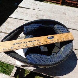 May include: A black motorcycle helmet with a blue and black padded interior. A ruler is placed across the helmet, measuring 19 inches.
