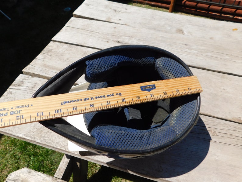 May include: A black motorcycle helmet with a blue and black padded interior. A ruler is placed across the helmet, measuring 19 inches.
