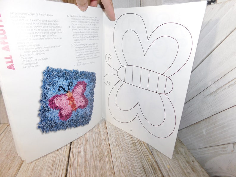 May include: A book with instructions on how to make a rug with a butterfly design. The book shows a finished rug with a blue background and a pink butterfly. The next page shows a line drawing of a butterfly.