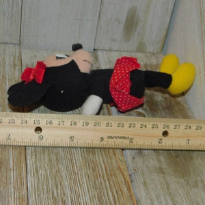May include: A black and red plush toy of Minnie Mouse, with a red bow and white polka dots on her skirt. The toy is about 15 inches long and is lying on a wooden surface.