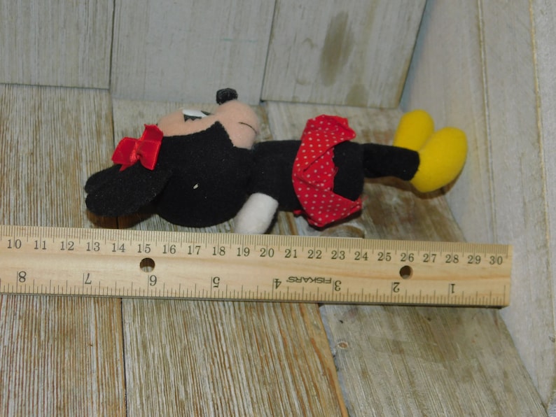 May include: A black and red plush toy of Minnie Mouse, with a red bow and white polka dots on her skirt. The toy is about 15 inches long and is lying on a wooden surface.