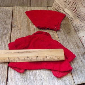 K&ouml;nnte beinhalten: Zwei rote Cordjacken f&uuml;r eine Puppe. Die gr&ouml;&szlig;ere Jacke liegt flach ausgelegt, die kleinere Jacke ist auf einem Holzlineal gefaltet. Das Lineal ist in Zoll eingeteilt.