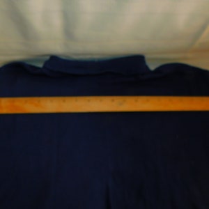 May include: A navy blue long-sleeved shirt with a wooden ruler placed across the back.