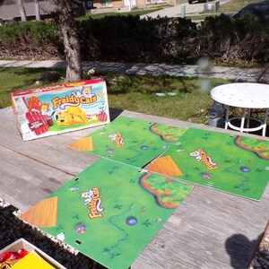 May include: A board game called "Fraidy Cats" with a green game board and a box with a yellow cat on it. The game board is made up of four pieces and has a blue, winding path on it.