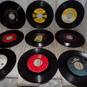 May include: A collection of ten 45 rpm vinyl records. The records are black with colorful labels. The labels feature the names of the artists and the titles of the songs. The records are arranged in two rows of five.