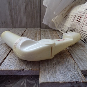 May include: White plastic hand-held device with a red label and a swiveling arm. The device is on a wooden surface.