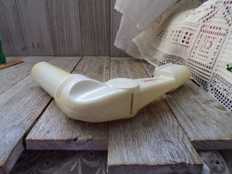 May include: White plastic hand-held device with a red label and a swiveling arm. The device is on a wooden surface.
