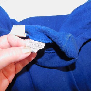 May include: Close-up of a blue fabric care label with the text "Machine Wash Lukewarm Gentle Tumble Dry Medium Move Immediately From Dryer To Prevent Wrinkles"