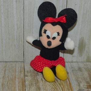 May include: A black and red plush toy of Minnie Mouse with a red bow and white polka dot skirt. The toy has large black eyes and a pink nose.