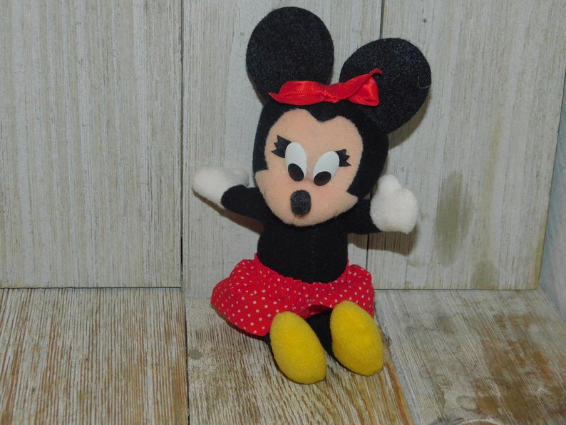 May include: A black and red plush toy of Minnie Mouse with a red bow and white polka dot skirt. The toy has large black eyes and a pink nose.