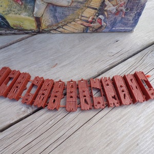 May include: A brown plastic bridge made of multiple pieces, each with a textured surface. The bridge is designed to be used with a board game.