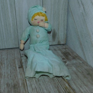 May include: A vintage blue and white fabric doll wearing a sleep cap. The doll is lying on its side with its head resting on its hand.