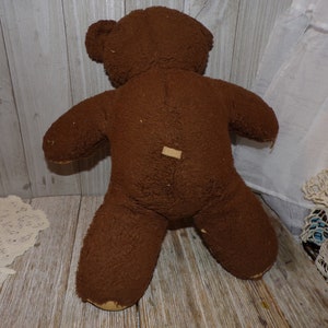 May include: A brown teddy bear with a worn, fuzzy texture. The bear is standing on a wooden surface.