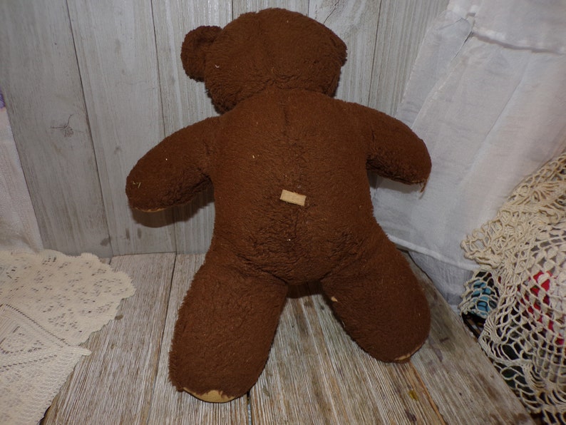 May include: A brown teddy bear with a worn, fuzzy texture. The bear is standing on a wooden surface.