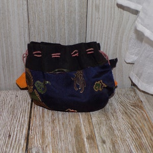 May include: A small drawstring bag with a black fabric top and a blue fabric bottom with a gold and green floral pattern. The bag has a pink drawstring and orange tassels.