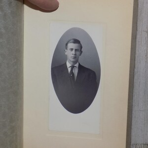 May include: A vintage black and white portrait of a man in a suit and tie, set within an oval frame. The photograph is mounted on a cream-colored background, suggesting an antique or historical context. The man is looking directly at the camera.