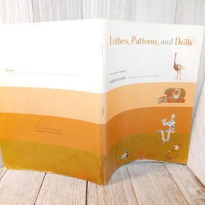 May include: A vintage book titled "Letters, Patterns, and Drills" with illustrations of an ostrich and other figures. The cover features a gradient of orange and white. The book is a third reader.