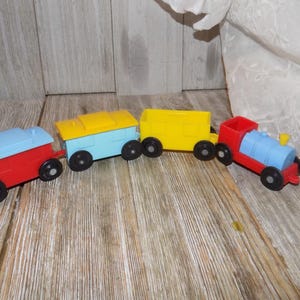 May include: A colourful toy train set with four connected carriages. The carriages are red, blue, yellow, and light blue. The train is on a wooden surface.