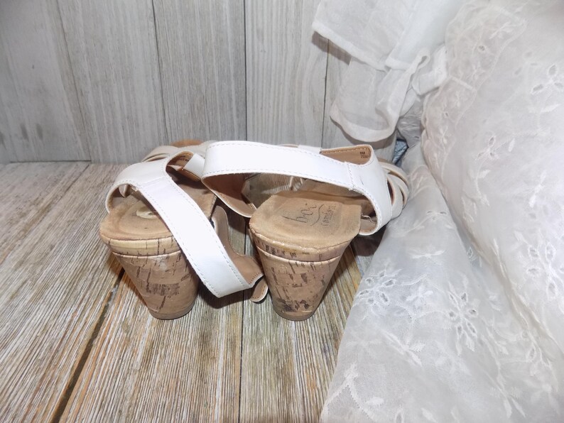 K&ouml;nnte beinhalten: Ein Paar wei&szlig;e Keilsandalen mit Korkabs&auml;tzen. Die Sandalen haben einen Riemen &uuml;ber dem Fu&szlig; und einen Kn&ouml;chelriemen.