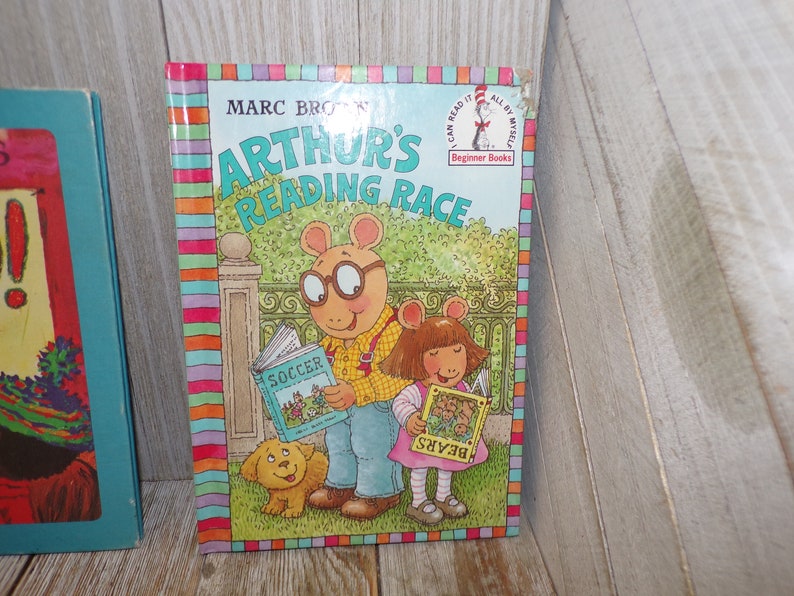 May include: A children's book titled "Arthur's Reading Race" by Marc Brown. The cover features Arthur and his sister D.W. reading books. Arthur is holding a book titled "Soccer" and D.W. is holding a book titled "Bears". The book is part of the "I Can Read It All By Myself" Beginner Books series.