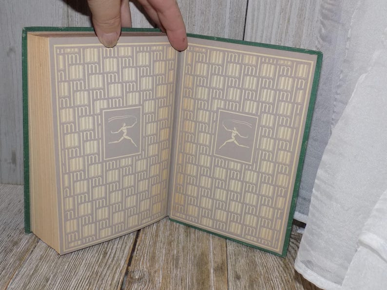 May include: A green hardcover book with a patterned design on the cover. The pattern is a series of small squares with a stylized figure in each square. The book is open to reveal the same pattern on the inside pages.