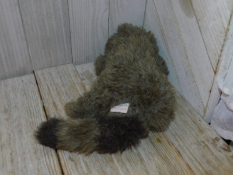 Puede incluir: Un juguete de peluche de mapache con pelaje marr&oacute;n y gris. El juguete tiene una peque&ntilde;a etiqueta en la espalda.