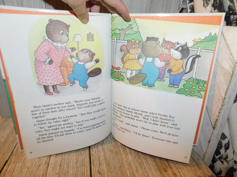 May include: A children's book illustration featuring a group of animal characters, including a beaver, a fox, a skunk, and a squirrel. The animals are standing in a backyard setting with a fence and flowers. The text on the page reads, "The next day at school Jamie asked Freddy Fox, Sandy Skunk, and Cindy Squirrel to come to his house to play. "Well, I don't know," said Cindy. "Teddy probably won't let us play with your toys anymore."  "But I will," said Jamie. "Please come. We'll all have fun."  "I'll be there." Everyone else said.
