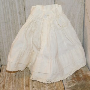 May include: A white cotton skirt with a button fastening and lace trim. The skirt is gathered at the waist and has a ruffled hem.
