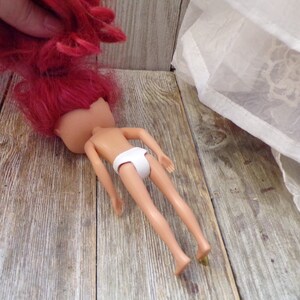 Pode incluir: Uma boneca com cabelo comprido e rosa brilhante deitada em uma superf&iacute;cie de madeira. A boneca est&aacute; sem cabe&ccedil;a e est&aacute; usando roupa interior branca.