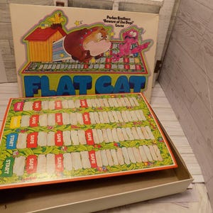 May include: A vintage Flat Cat board game by Parker Brothers featuring a colorful game box lid with a cartoon dog and cat illustration, and a rectangular game board with four start positions, red safe zones, and a green grassy path design.